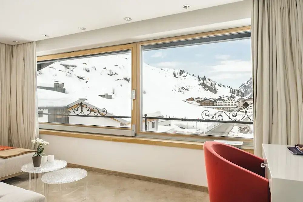 Großes Fenster mit beeindruckendem Blick auf die schneebedeckten Berge und ein roter Sessel.