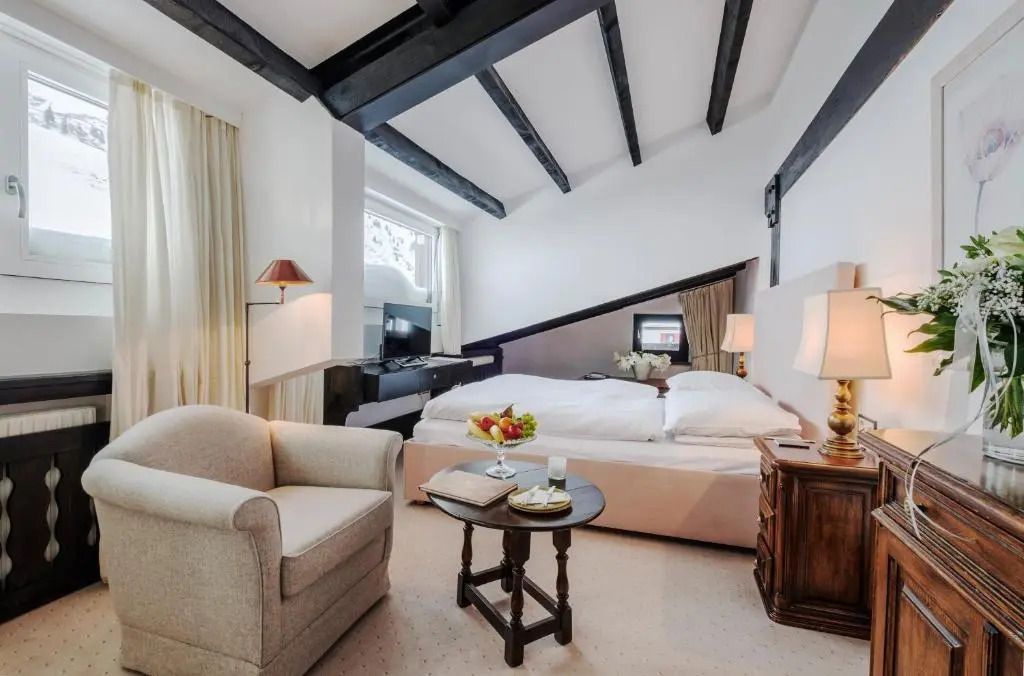 Gemütliches Zimmer mit Holzbalken, Doppelbett und Sesseln