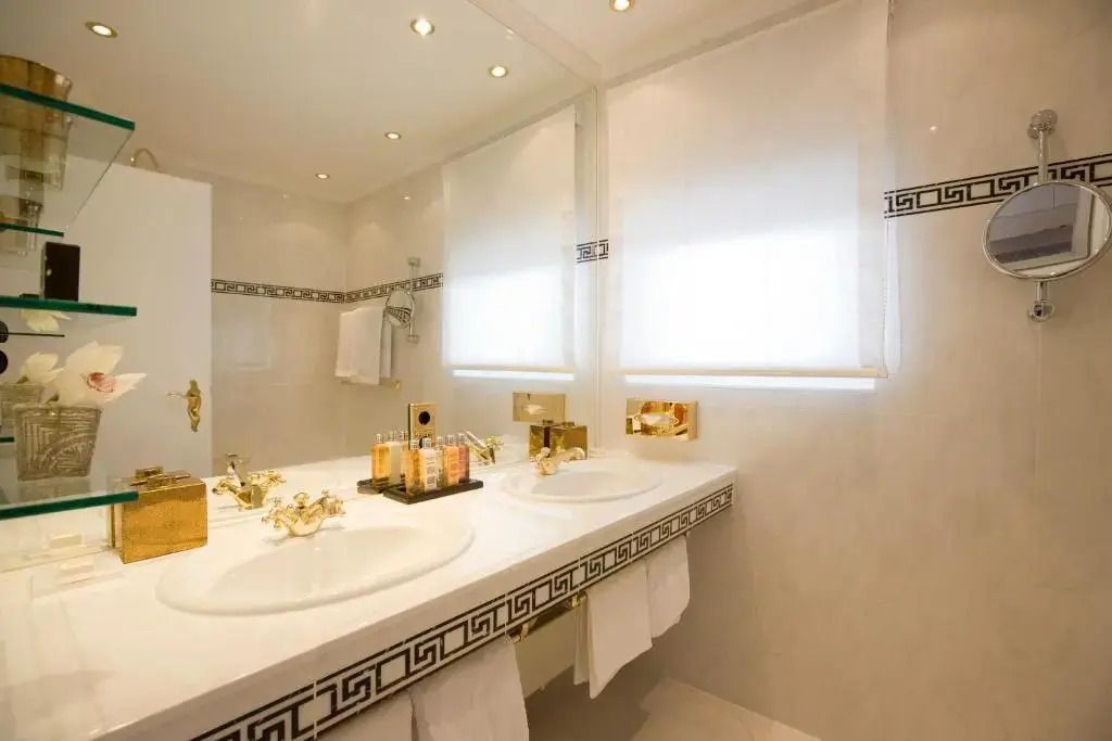 Luxuriöses Badezimmer mit Doppelwaschbecken und goldenen Armaturen in Suite