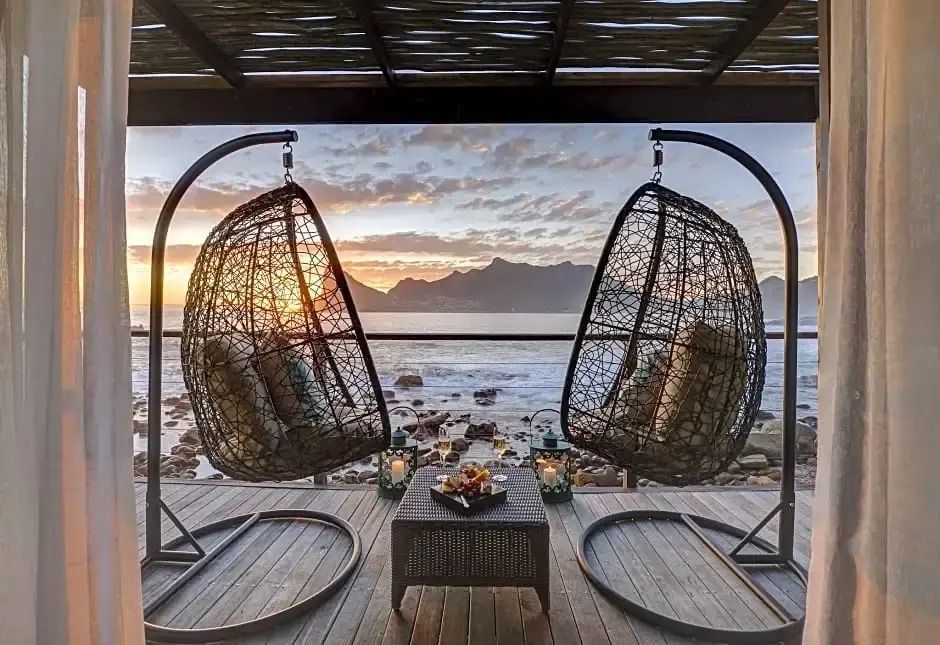 Zwei hängende Stühle auf einer Terrasse mit Meerblick und Sonnenuntergang.