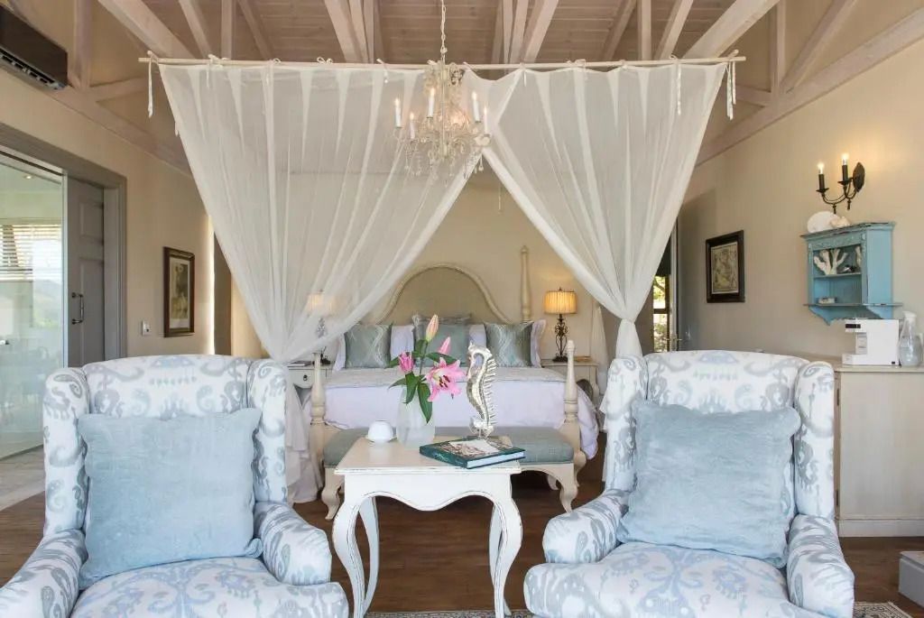 Schlafzimmer mit Himmelbett, eleganten Sesseln und Blumenstrauß