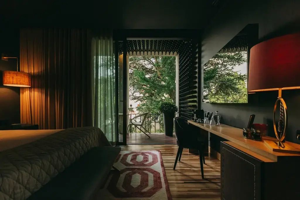 Hotelzimmer mit Zugang zu einem Balkon mit Blick auf Bäume und natürlichem Licht.
