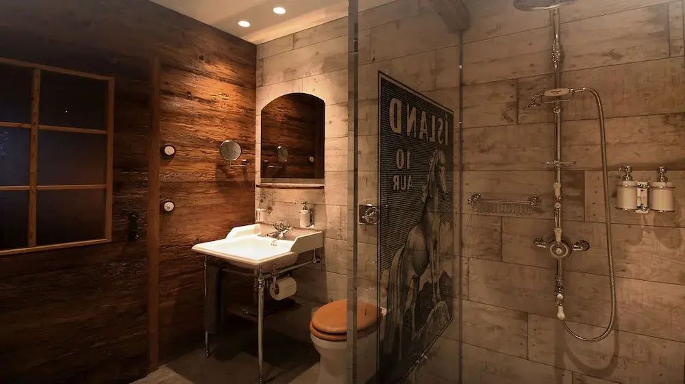Rustikales Badezimmer im Torfhús Retreat mit Holzverkleidung, Glasdusche und edlem Waschbecken.