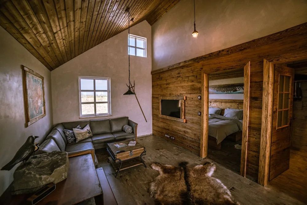 Geräumiges Wohnzimmer der Villa mit Ledercouch, Fellteppich und Blick ins Schlafzimmer.
