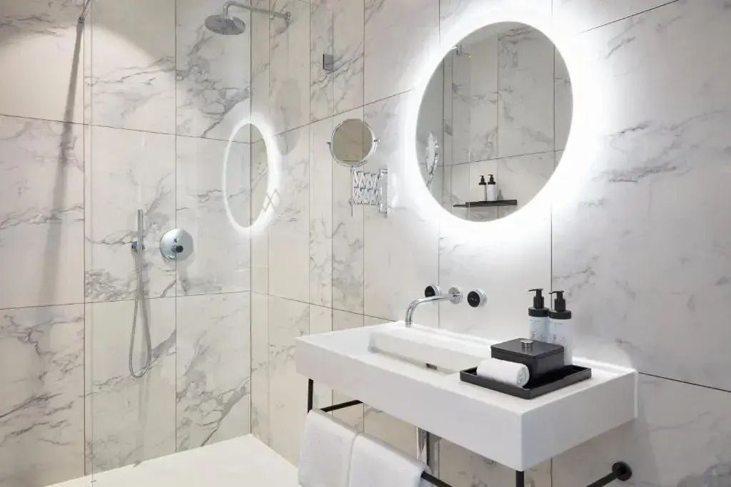 Modernes Badezimmer mit Marmorfliesen, Rundspiegel und Duscheinrichtung.