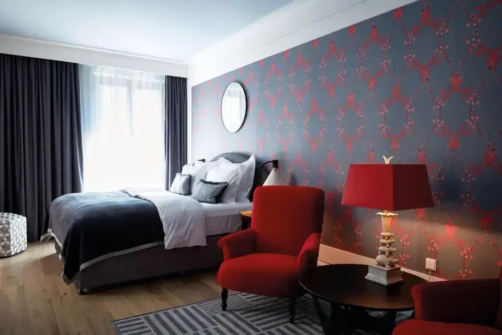 Elegantes Schlafzimmer mit Doppelbett, rotem Sessel und gemusterter Tapete