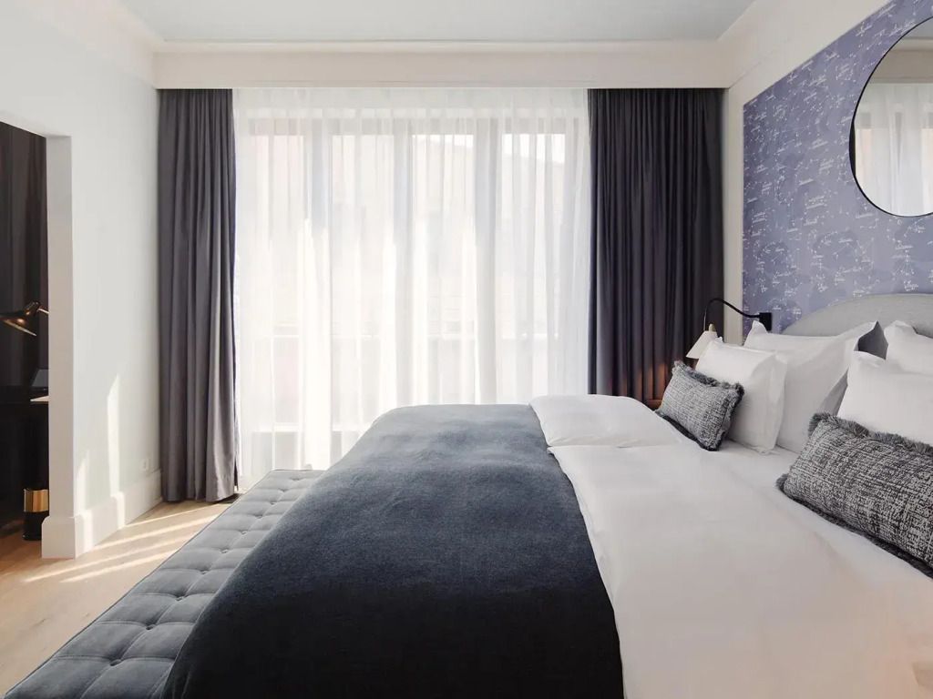 Helles Zimmer mit großem Doppelbett und Fensterfront mit Vorhängen