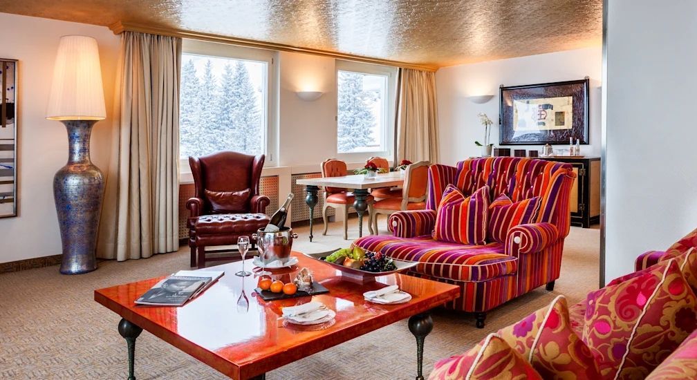 Wohnbereich der Suite mit farbenfrohem Sofa und Aussicht auf verschneite Bäume.