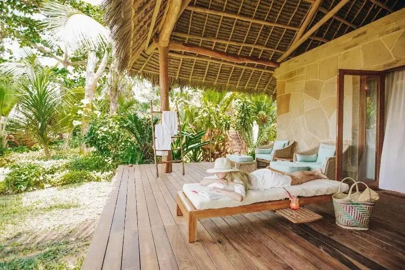 Holzterrasse mit Liege und Gartenblick im Deluxe Bungalow des Tulia Zanzibar Resorts