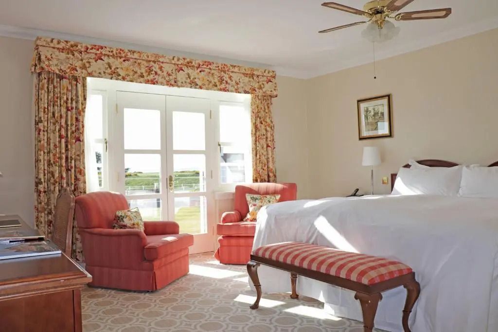 Helles Schlafzimmer mit Doppelbett und Sitzbereich mit Blick auf den Golfplatz.