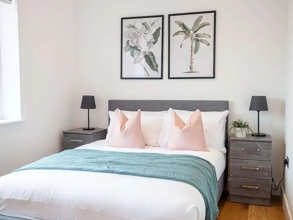 Modernes Schlafzimmer mit grauem Bett und botanischer Kunst an der Wand.