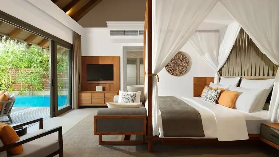 Helles Schlafzimmer mit Himmelbett und Holzdekor im Vakkaru Maldives, Blick auf den Pool.
