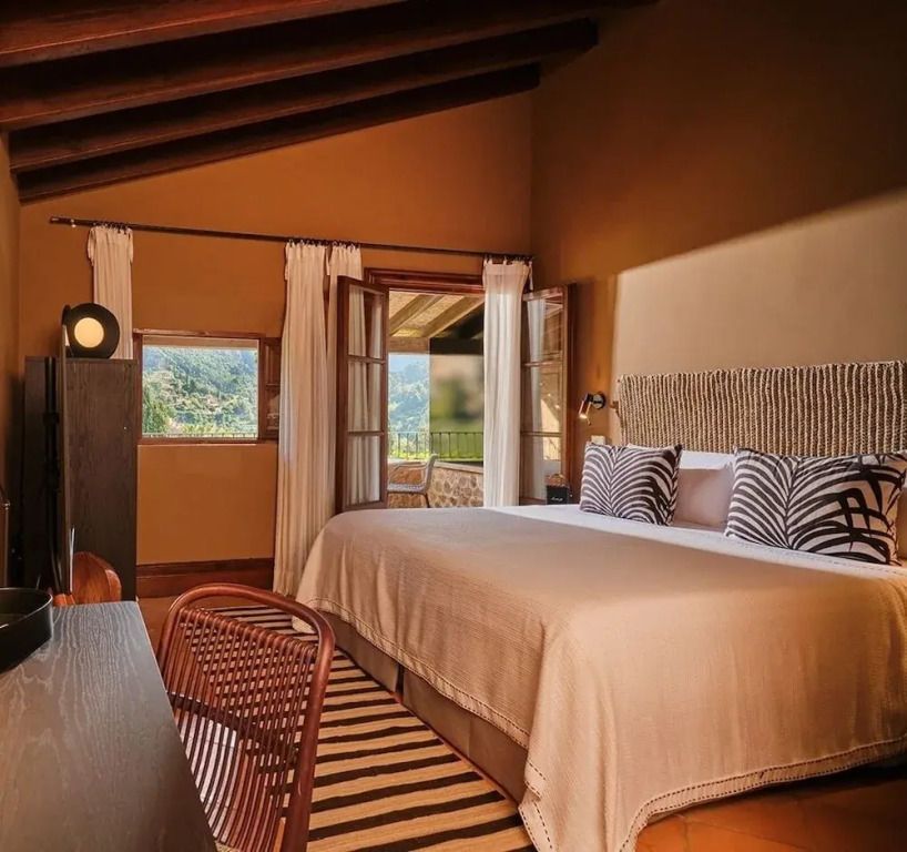 Deluxe Zimmer mit großem Bett, Holzbalkendecke und Ausblick auf die Landschaft.