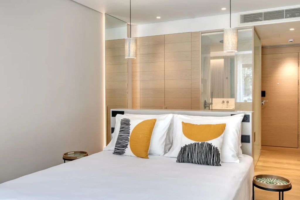 Modernes Schlafzimmer mit Doppelbett, stilvollen Kissen und heller Beleuchtung.