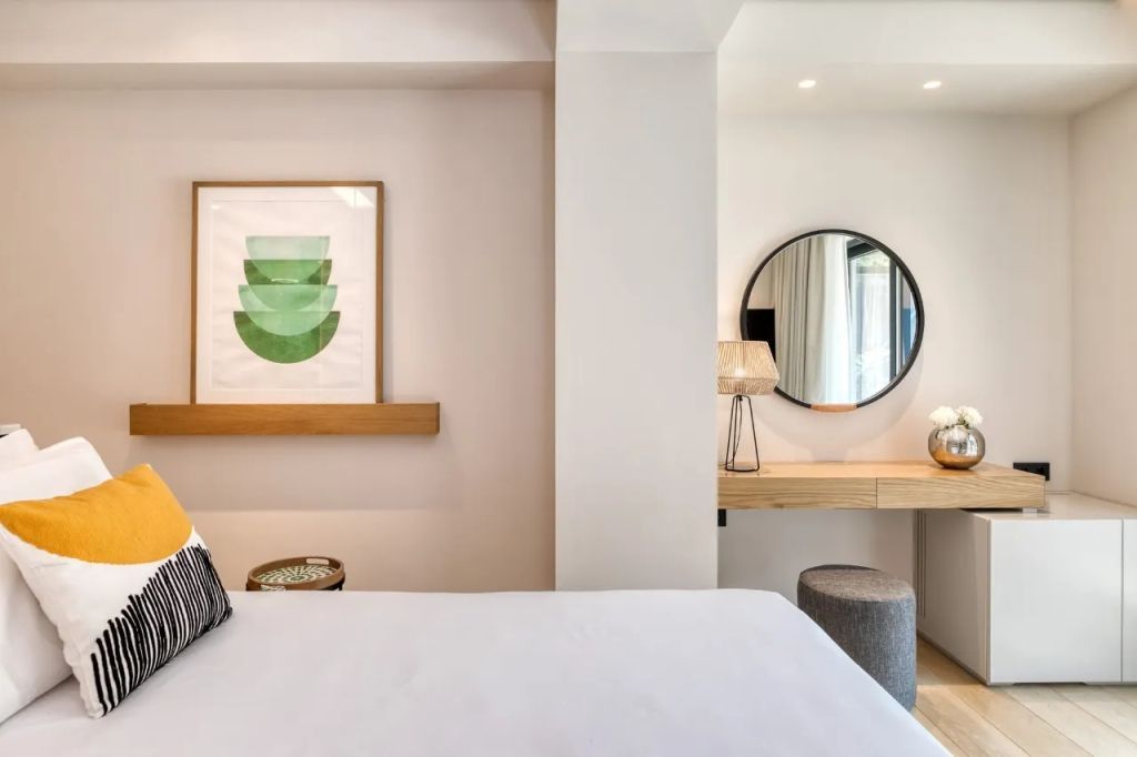 Schlafzimmer mit Kunstwerk an der Wand, rundem Spiegel und Holzmöbeln.