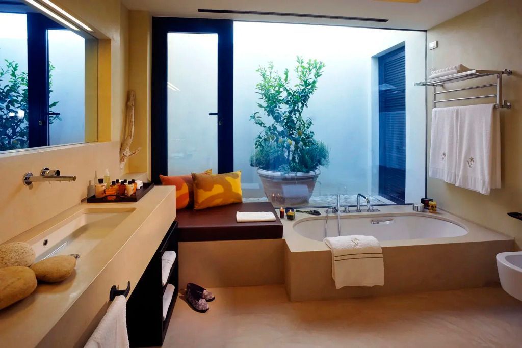 Modernes Badezimmer mit großer Badewanne und Blick auf Innenhof mit Pflanze