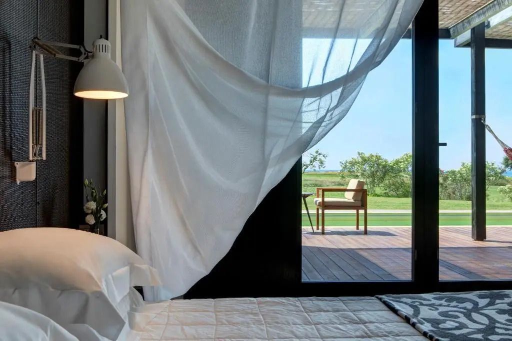 Helles Schlafzimmer mit fließendem Vorhang und Blick auf Terrasse und Garten