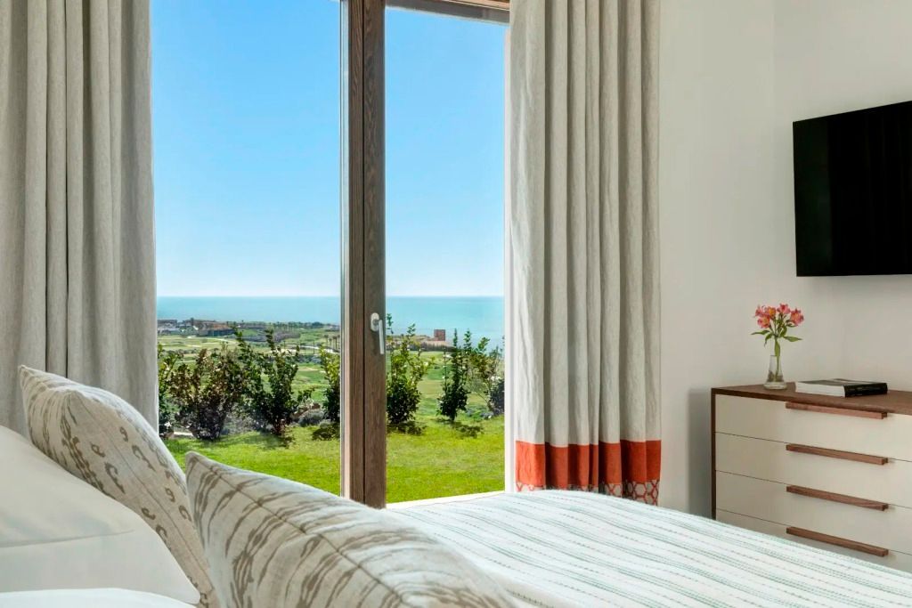 Schlafzimmer mit Meerblick im Verdura Resort, helle Vorhänge und Tür zum Garten