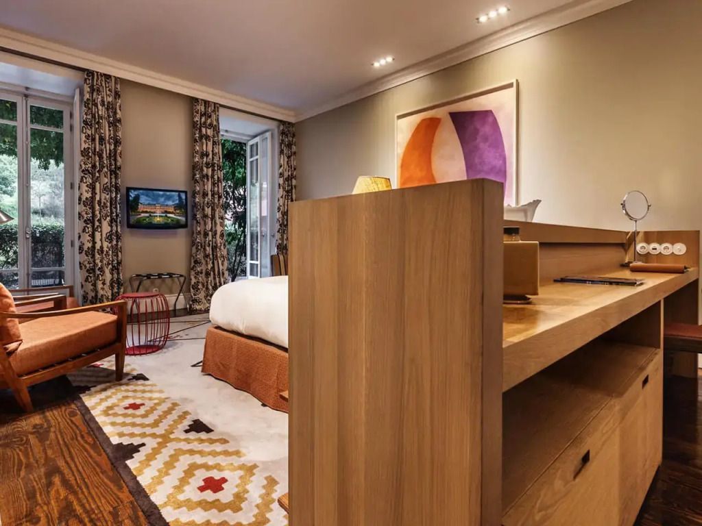 Gemütliches Deluxe Zimmer mit Holzmöbeln und Zugang zu einem Balkon mit üppigem Gartenblick.