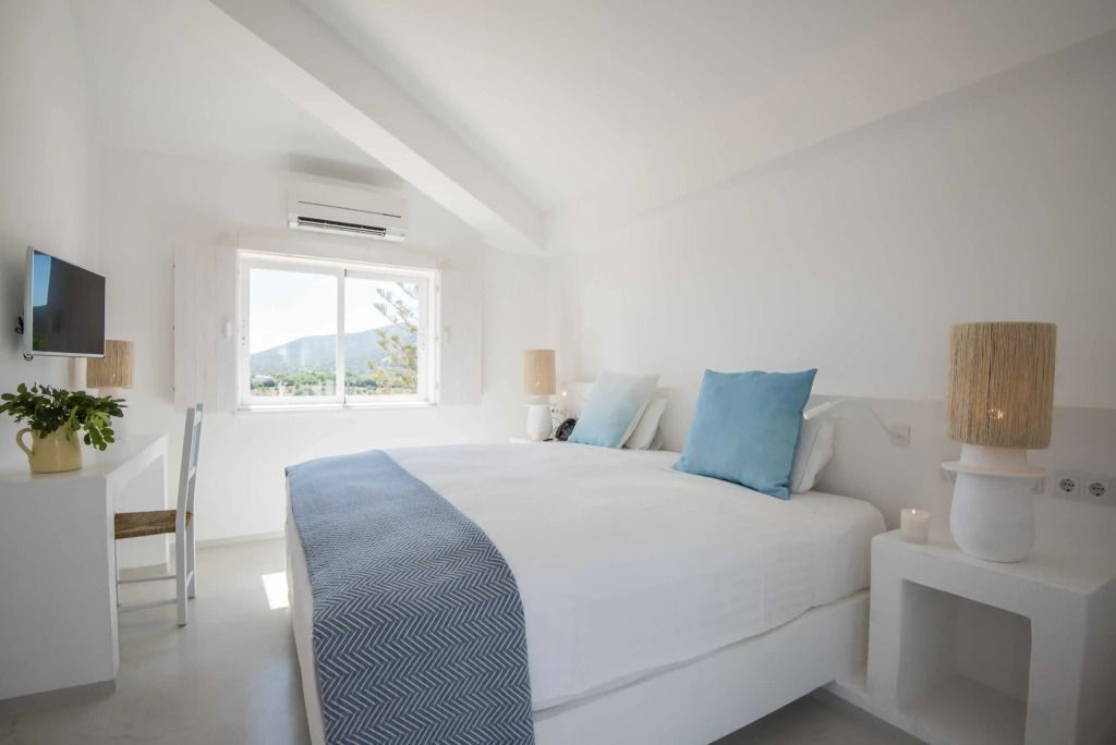 Helles Schlafzimmer mit Doppelbett, großem Fenster und minimalistischer Einrichtung.