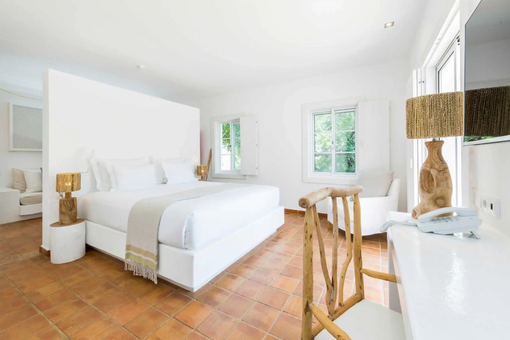 Schlafzimmer mit großem Bett und Terrakotta-Fliesen, umgeben von Fenstern.
