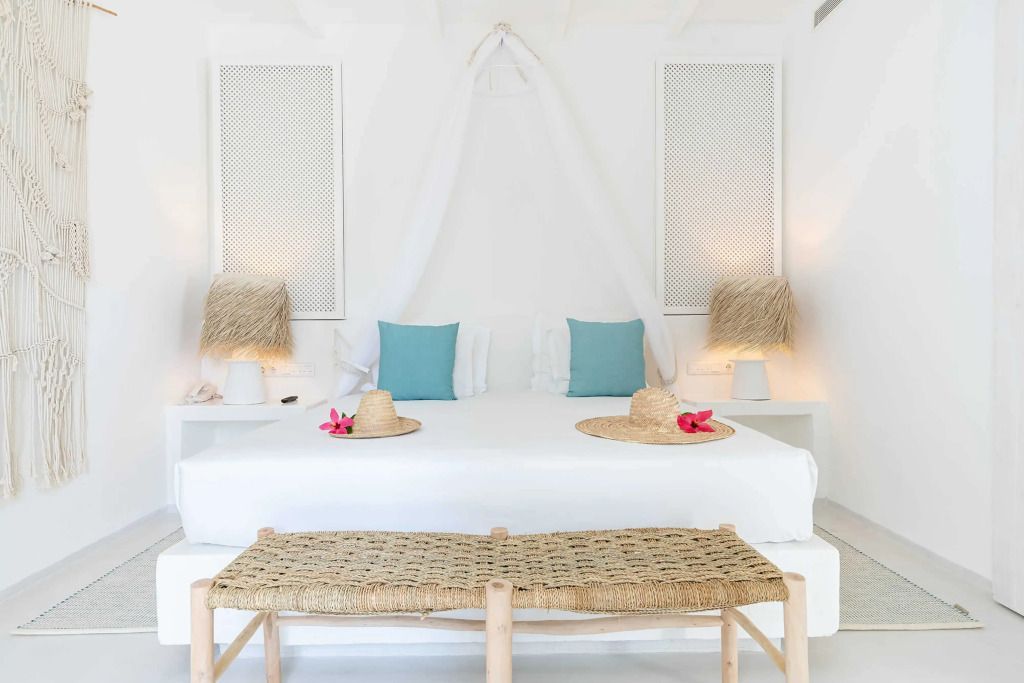 Doppelbett mit blauen Kissen und Strohhüten in hellem Zimmer