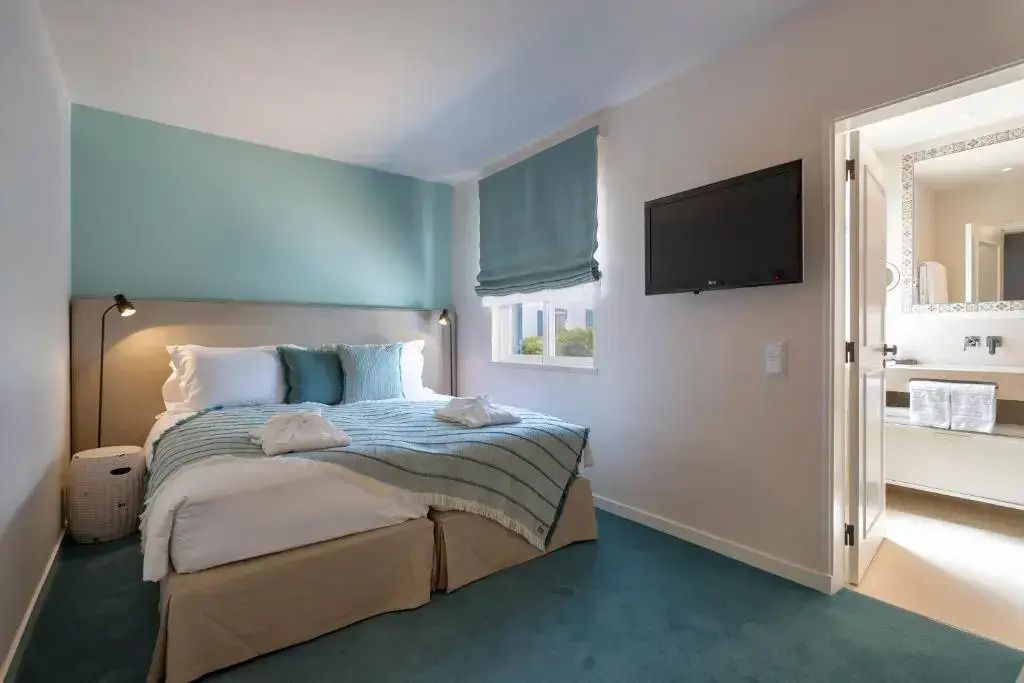 Helles Schlafzimmer mit Doppelbett und Blick auf den Flachbildfernseher.
