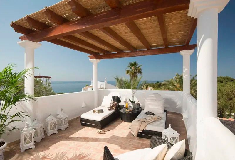 Terrasse mit Meerblick und luxuriösen Sonnenliegen unter einer Holzpergola