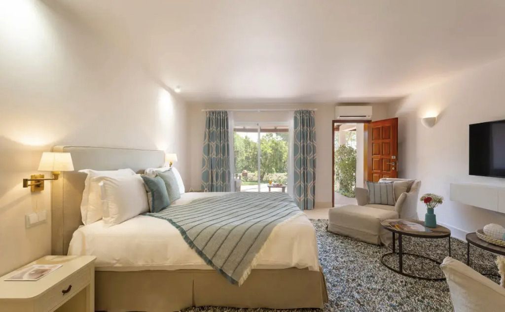 Geräumiges Schlafzimmer mit großem Bett Blick auf Terrasse und Garten durch eine Glastür