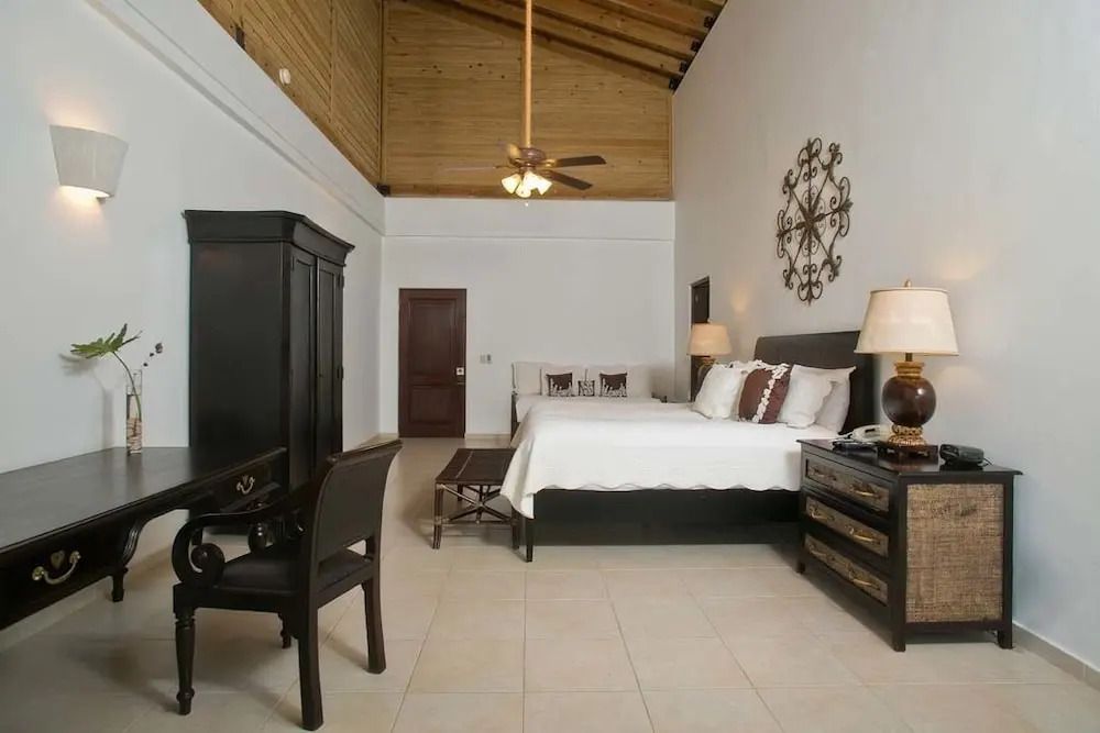 Helles Schlafzimmer mit hoher Holzdecke, Doppelbett, Schreibtisch und stilvollen Dekorationen.