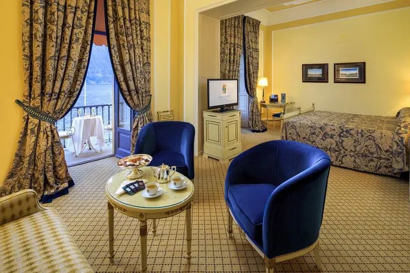 Junior-Suite mit eleganten blauen Sesseln, Blick auf den See durch große Fenster.