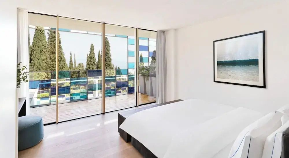 Schlafzimmer mit großem Bett und Glasfront zu einer bunten Terrasse