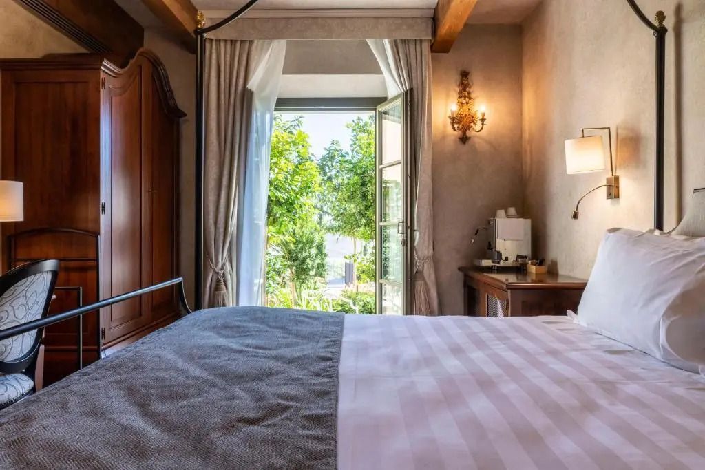 Junior-Suite mit Bett, offenem Fenster und Blick auf grüne Umgebung