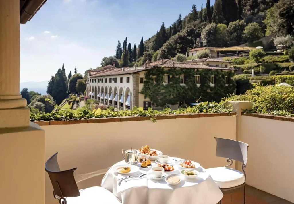 Terrasse mit gedecktem Frühstückstisch vor toskanischem Gebäude und Hügellandschaft