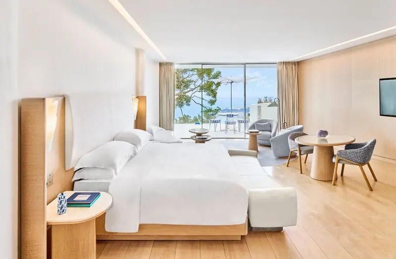 Helles Schlafzimmer mit Doppelbett und Meerblick durch große Glasfenster