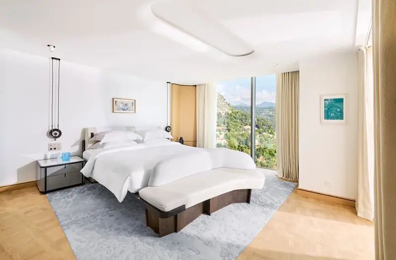 Großes Doppelbett in moderner Suite mit Panoramafenster und Blick auf die Landschaft