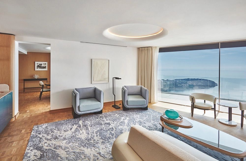 Elegante Suite mit Sitzbereich vor einem großen Fenster mit Meerblick
