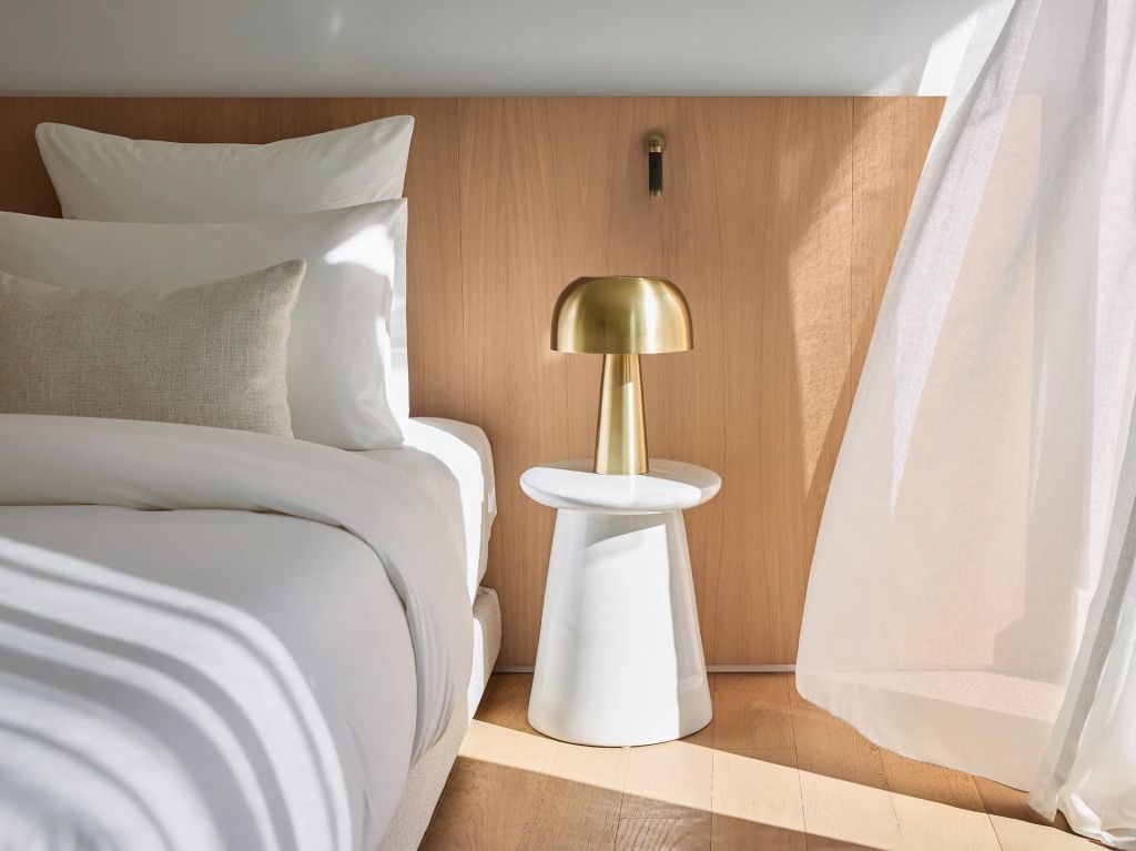 Hochwertiges Doppelzimmer mit Bett aus weißer Bettwäsche und goldener Nachttischlampe