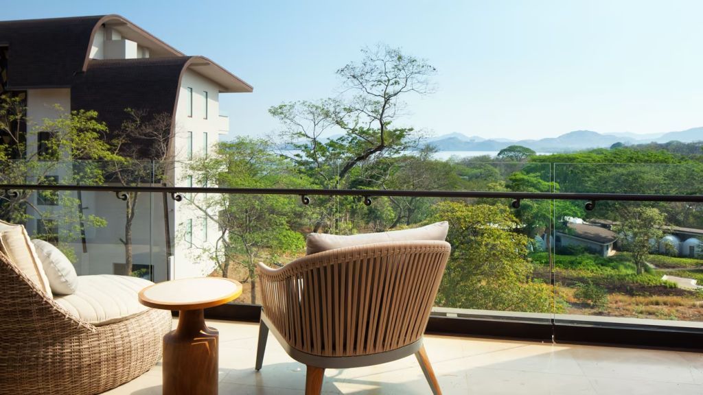 Balkon mit Sitzgelegenheit und Blick auf üppiges Grün und das Meer.