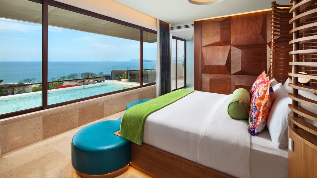 Geräumiges Schlafzimmer mit Panoramafenster und Blick auf den Infinity-Pool.