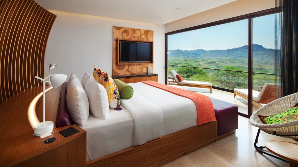 Helles Zimmer mit Doppelbett, TV und großem Fenster mit Blick auf grüne Hügel