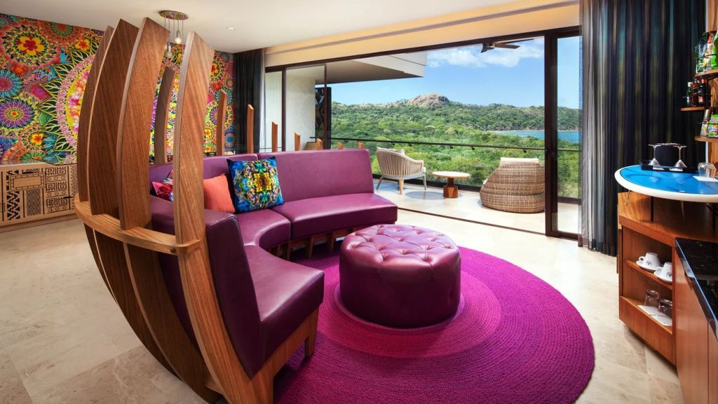 Sitzecke in der Suite mit violetten Möbeln und Fensterblick auf Hügel