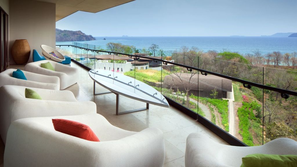 Privater Balkon mit Sitzgelegenheiten und Surfboard, Blick auf das Meer.