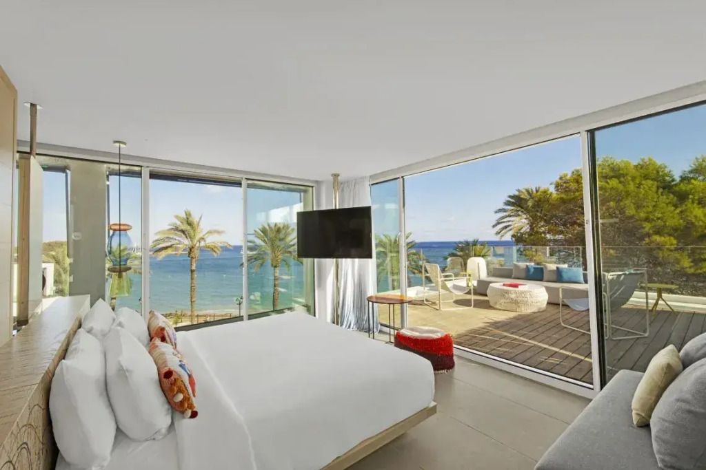 Helle Suite mit Doppelbett, großen Fenstern und Meerblick auf Palmen und Strand