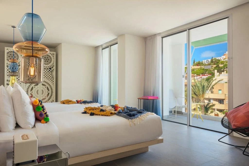 Helle Suite mit zwei Einzelbetten und Balkon mit Meerblick, stilvolle Dekoration.