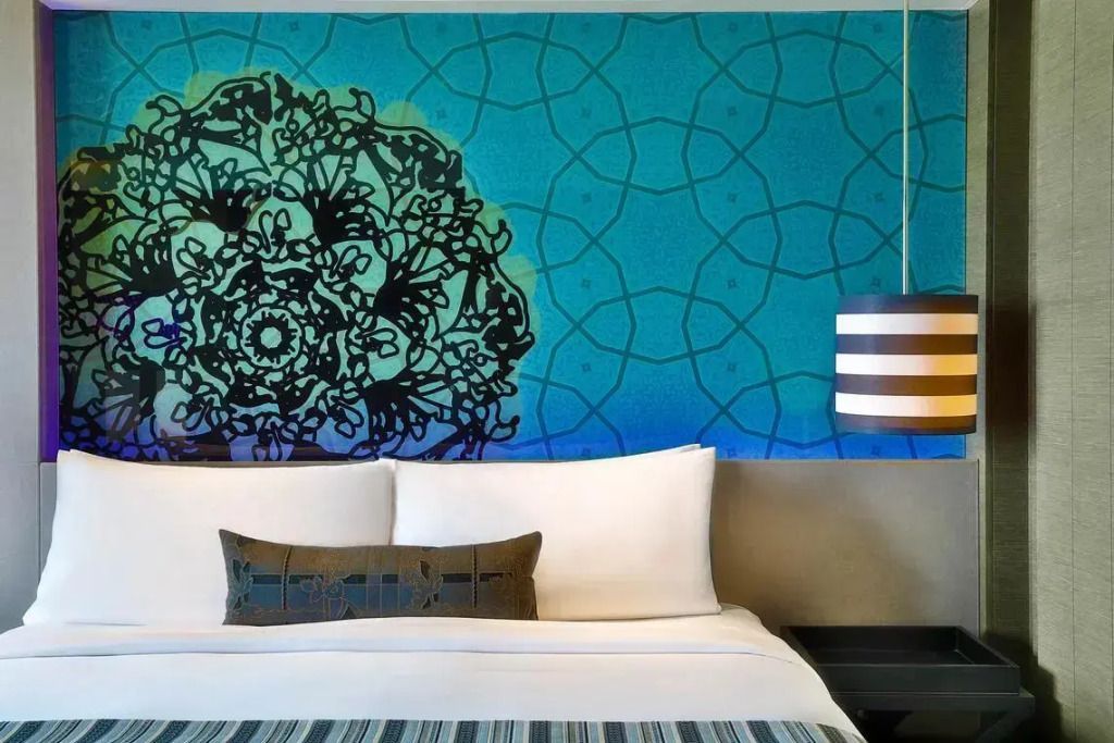 Detailansicht eines Doppelbetts mit künstlerischem Wanddesign und eleganter Lampe.
