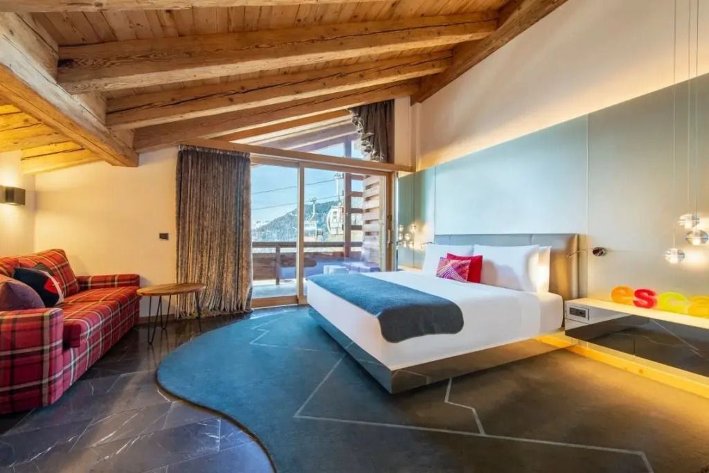 Helle Junior-Suite mit Holzbalkendecke und großem Fenster mit Bergblick.