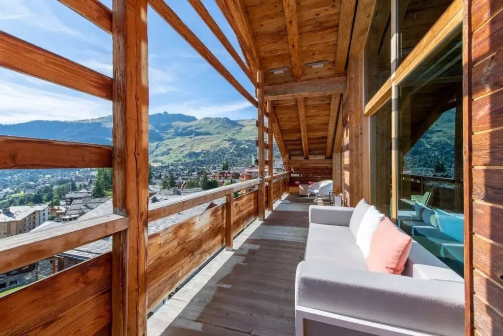 Holzbalkon mit Sitzgelegenheiten und Blick auf grüne Sommerberge.