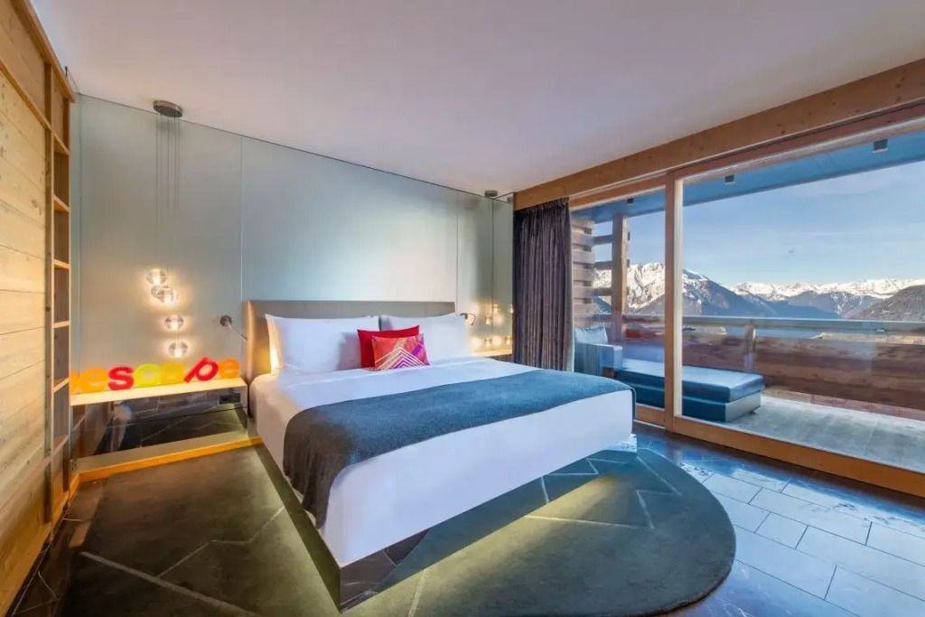 Geräumiges Zimmer mit Doppelbett und Blick auf verschneite Berge vom Balkon.