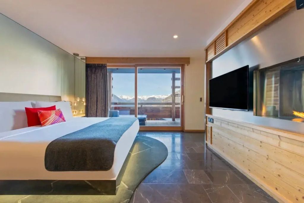 Modernes Doppelzimmer mit großem TV und Bergblick durch die Glasfront.